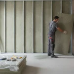 Artisan posant des panneaux d'isolation thermique en laine de roche sur un mur intérieur, chantier de rénovation énergétique